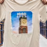 A beige t-shirt featuring a clock tower and text that reads "1994. Taylor's version."